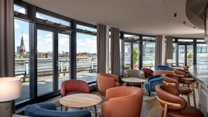 Un moderno vestíbulo de hotel con amplios ventanales, zonas de estar y vistas a la ciudad.
