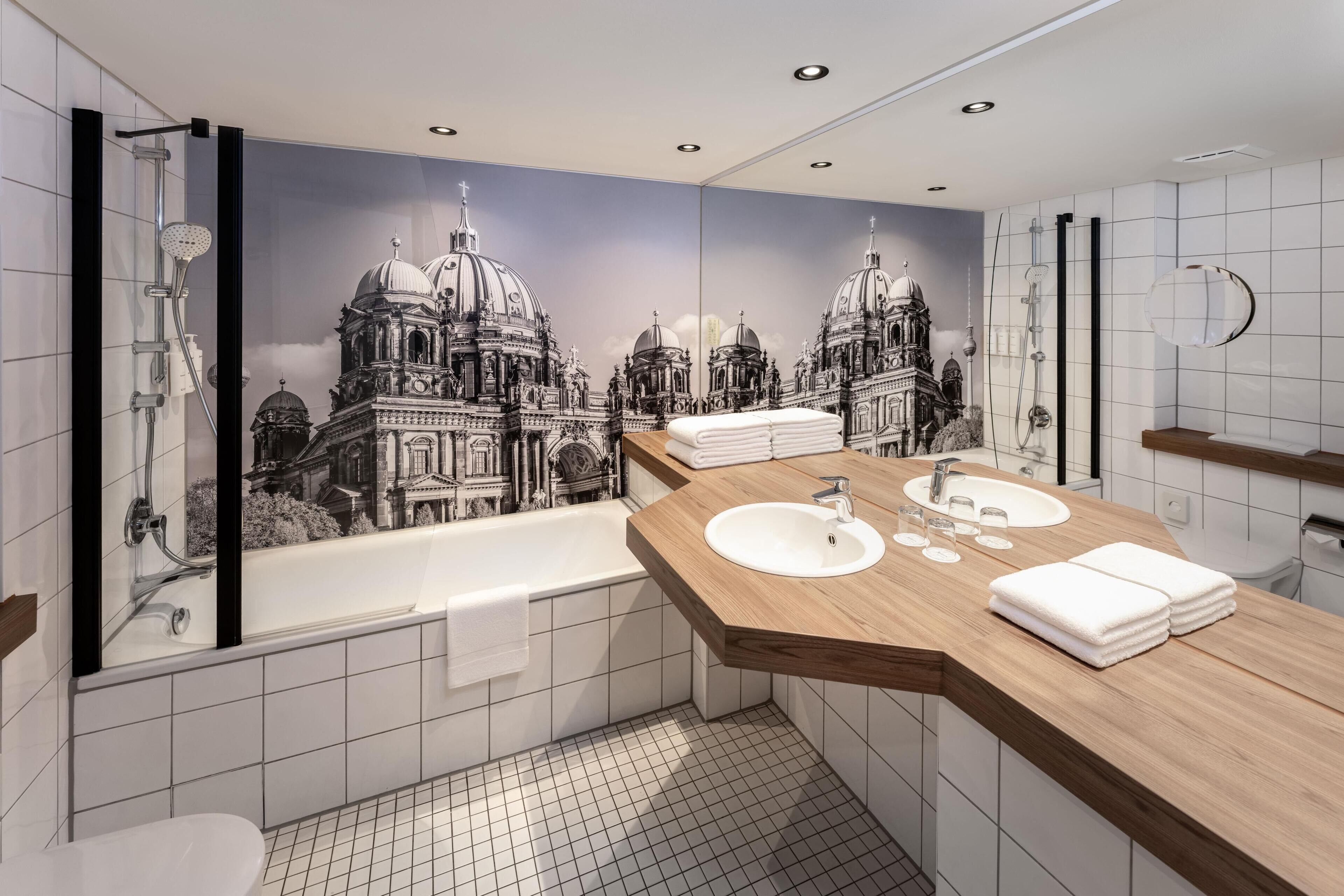 A modern bathroom with a large mirror, two sinks, a bathtub, and a shower.