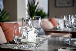 Un tavolo da pranzo con diversi bicchieri da vino e piatti, in una stanza che include un divano e una pianta sullo sfondo.