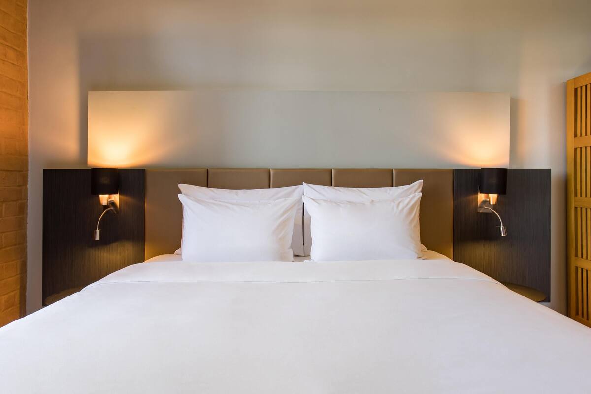 Una habitación de hotel con una cama grande, dos lámparas de noche y un cabecero de madera.