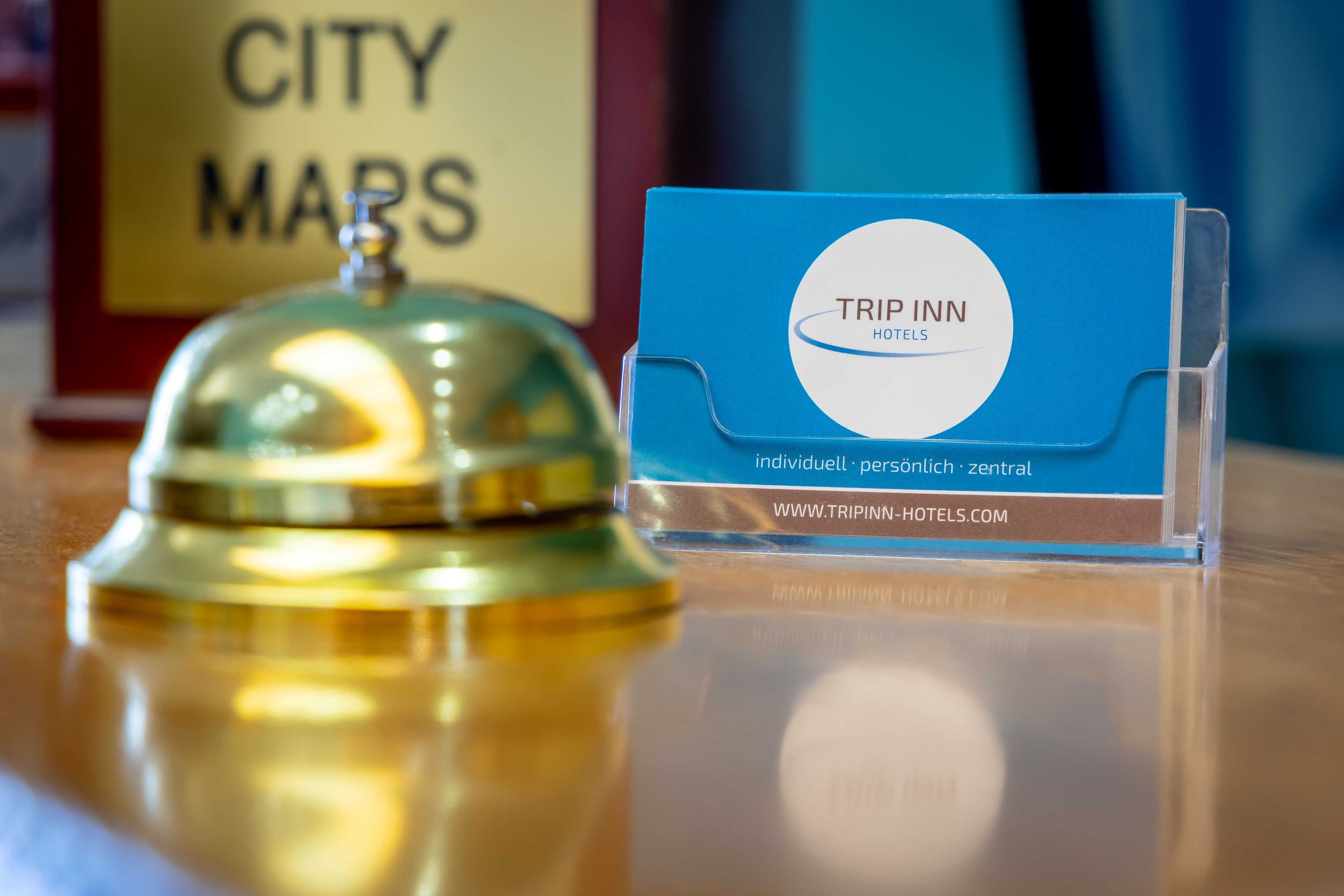 A blue business card for Trip Inn Hotels with a website URL and a sign for City Maps in the background.