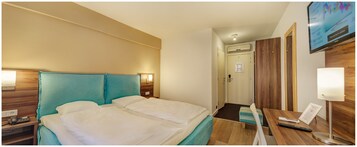 Habitación de hotel con cama, mesitas de noche, escritorio, silla, televisor y puerta.