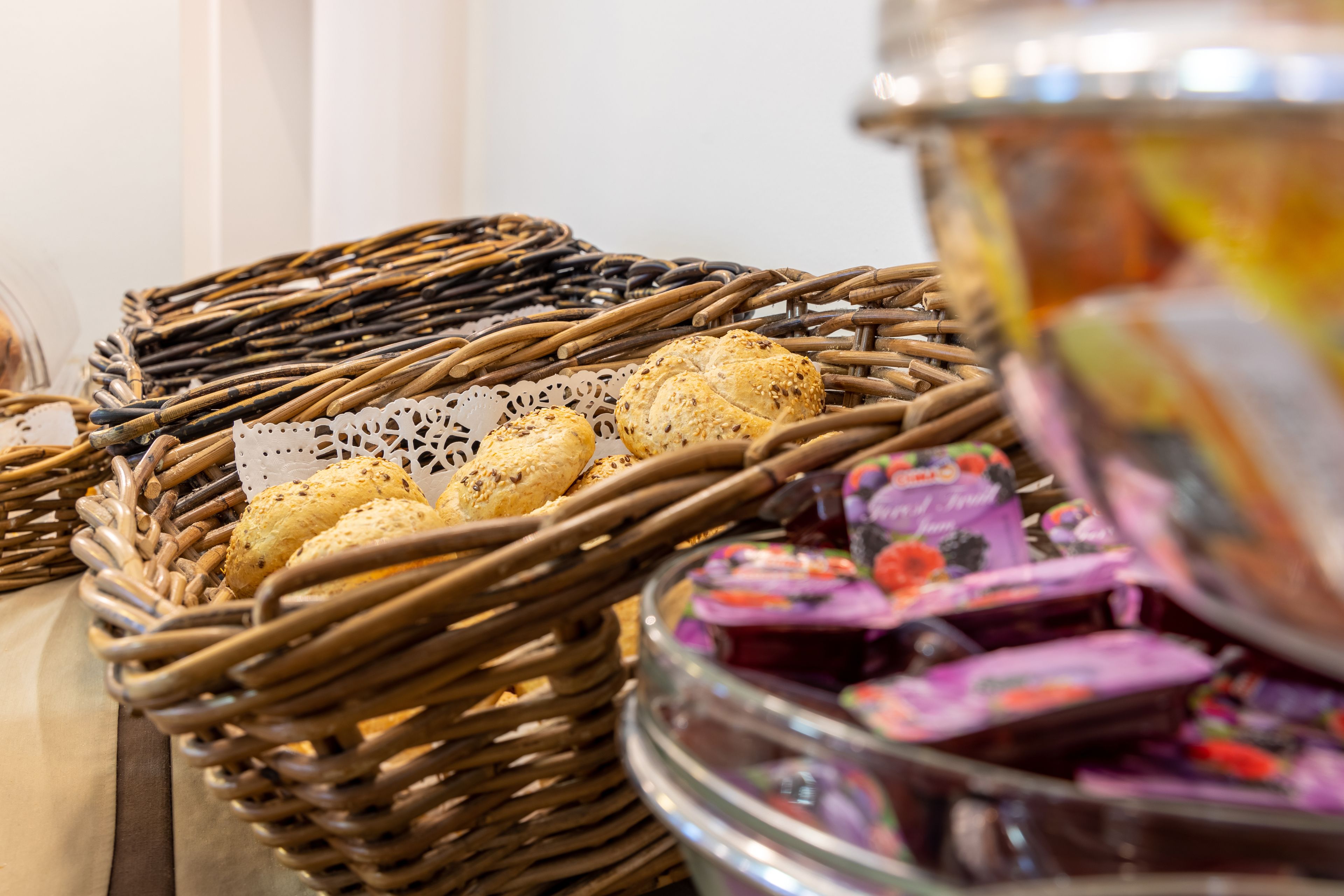 A wicker basket with bread and a glass jar of jam.