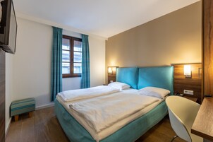 Una habitación de hotel con cama, escritorio, silla, televisor y ventana con cortinas.