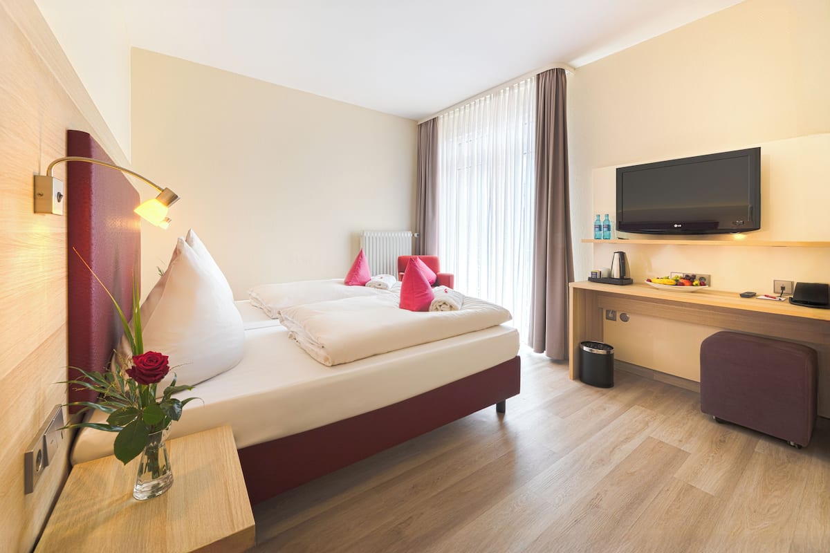 A hotel room with a bed, a desk, a TV, and a vase with a flower.