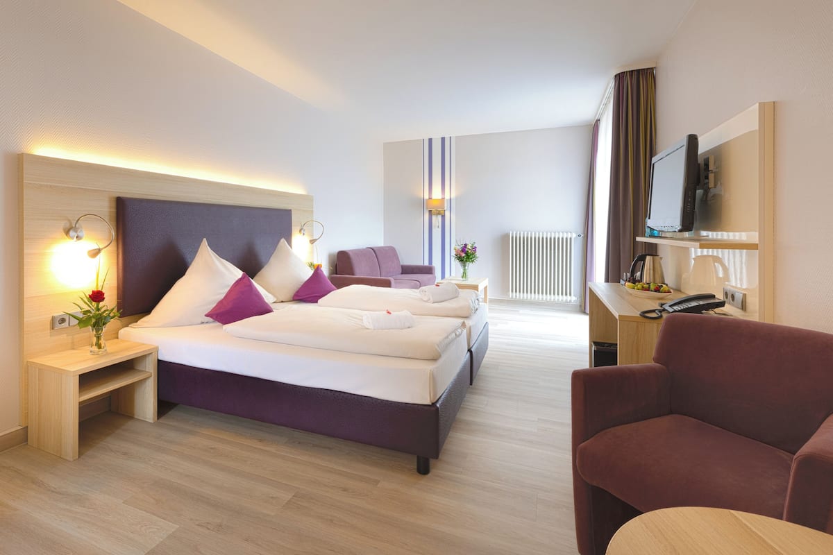A modern hotel room with a large bed, a desk with a computer, and a seating area.