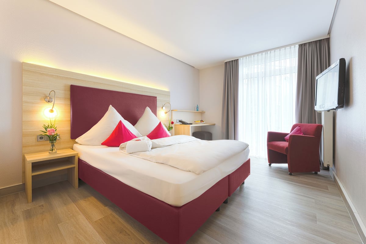 A hotel room with a large bed, a desk, a chair, and a TV mounted on the wall.
