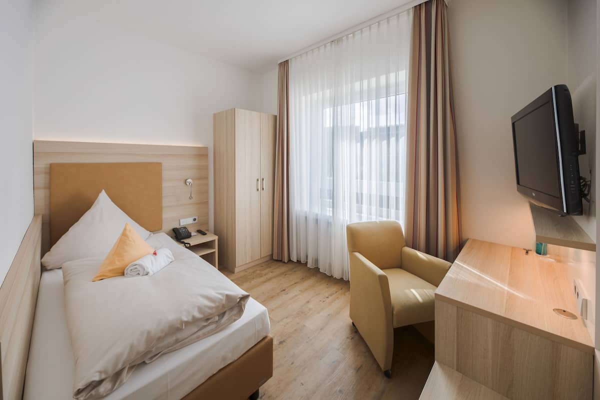 A hotel room with a bed, a desk, a chair, a wardrobe, and a television.