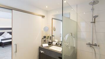 A modern hotel bathroom with a glass shower enclosure, a large mirror, and a vanity with a sink and towel.