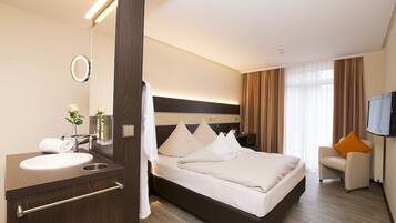A hotel room with a large bed, a bedside table, a mirror, a TV, and a seating area with a chair and a sofa.