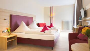 A modern hotel room with a large bed, a wooden nightstand, a desk, and a red armchair.