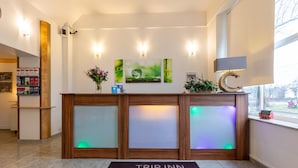 Um balcão de recepção com divisória de vidro, um letreiro com a inscrição “TRIP INN” e uma janela com vista.