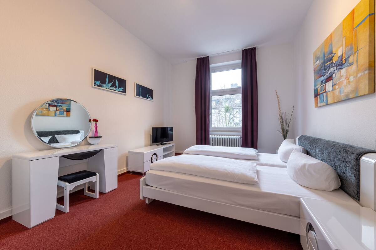 A hotel room with a bed, a desk with a mirror, a television, and artwork on the walls.