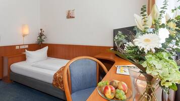 Ein Hotelzimmer mit einem Bett, einem hölzernen Schreibtisch mit Blumen und einer Obstschale.