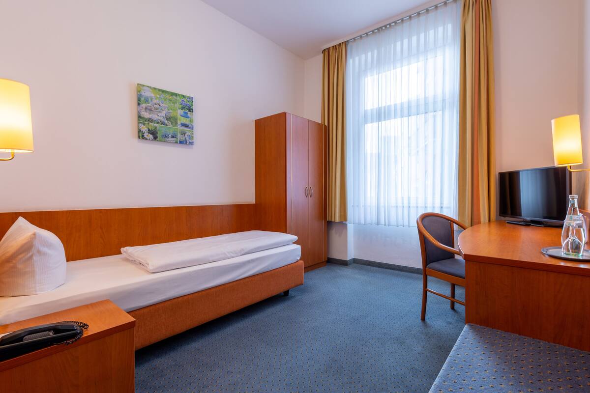 A hotel room with a single bed, a desk with a chair, a television, and a telephone.