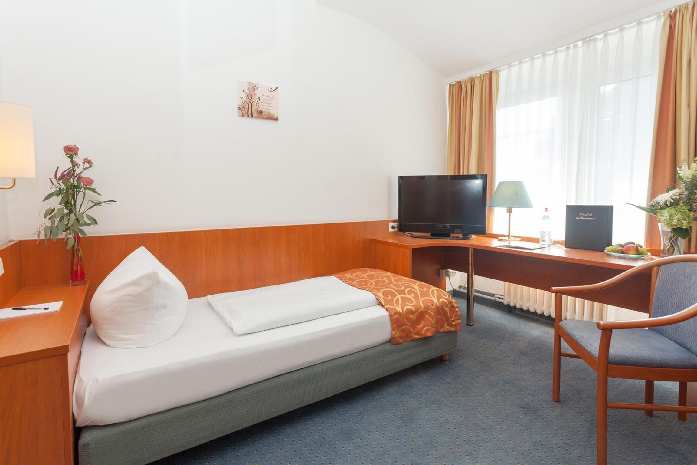A hotel room with a single bed, a desk with a computer, a television, and a chair.