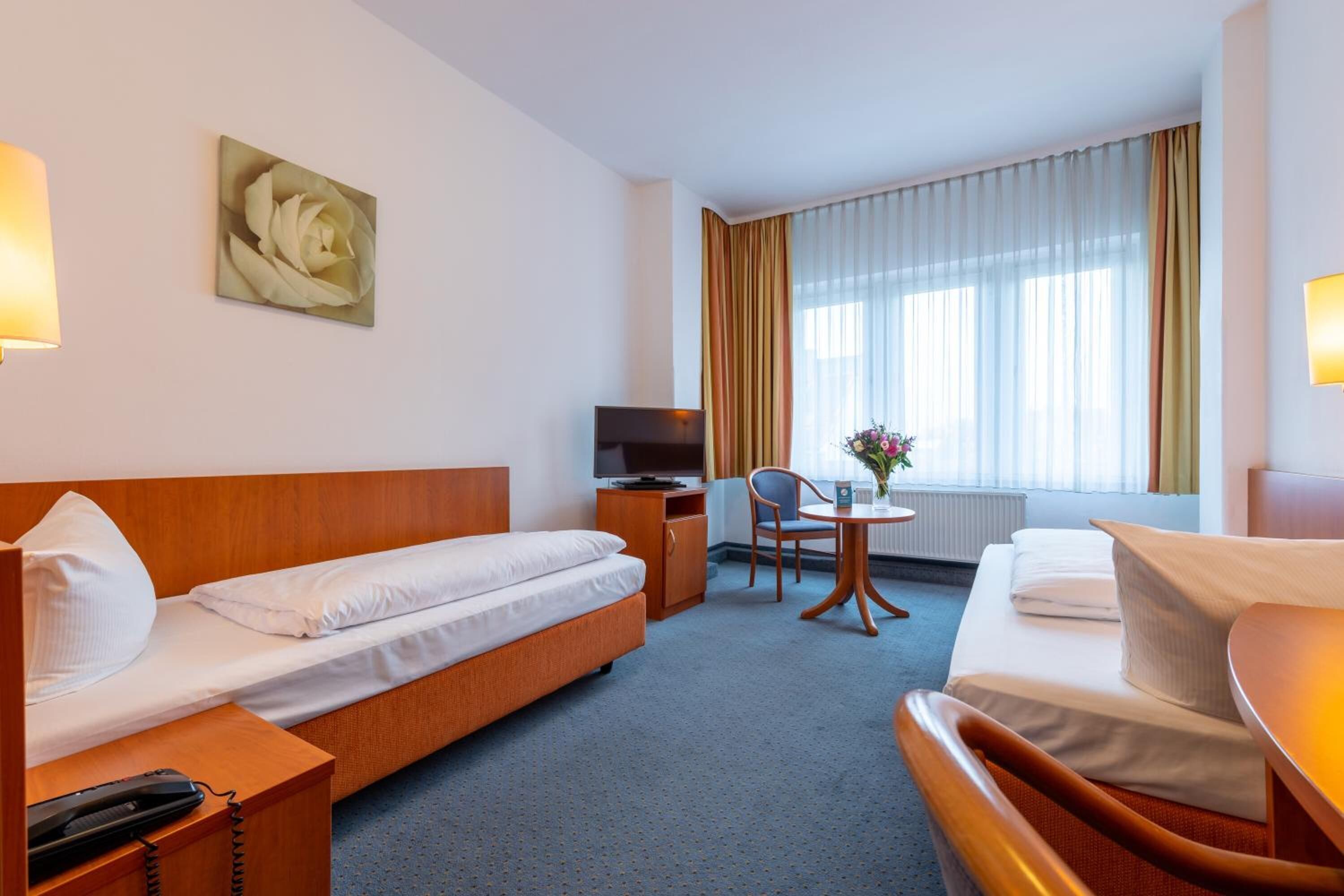 Ein Hotelzimmer mit Bett, einer Couch, einem Schreibtisch mit Lampe, einem Fernseher und einem Fenster mit Vorhängen.