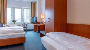 Quarto de hotel com uma cama, uma escrivaninha com computador, televisão e janela com cortinas.