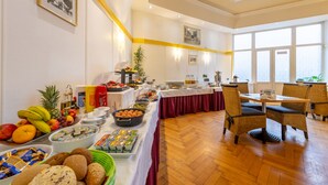 Disposição de buffet com diversos alimentos e área de estar com cadeiras de vime.
