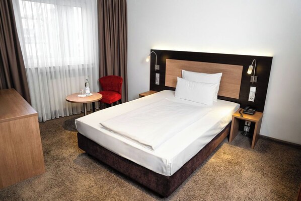 Habitación de hotel con una cama grande, un escritorio, una silla y una mesita.