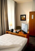 A hotel room with a bed, a desk with a laptop, a chair, a lamp, and a door.