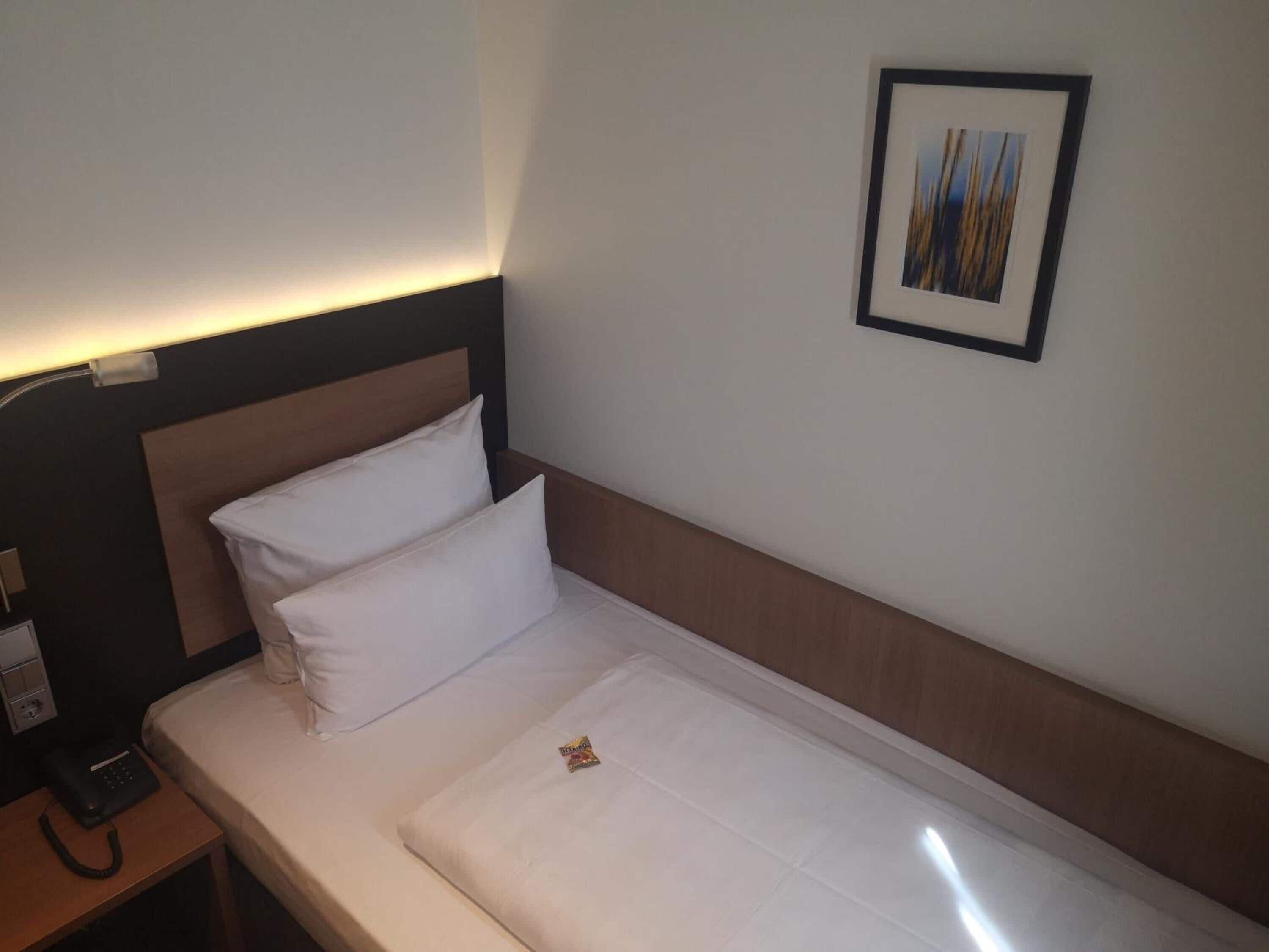 A hotel room with a single bed, a bedside telephone, and a framed picture on the wall.