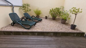 Un espace patio comprenant deux fauteuils de jardin verts, un sol en gravier et plusieurs plantes en pot.