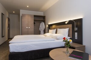 Ein Hotelzimmer mit einem Doppelbett, einem Nachttisch mit einem Buch, einem Schrank und einem Spiegel.