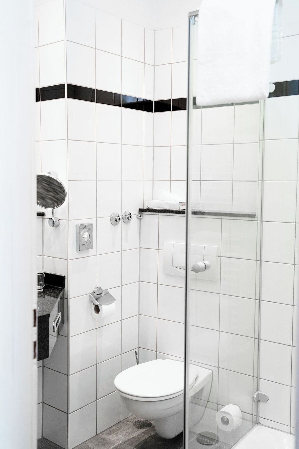 A modern bathroom with white tiles, a glass shower enclosure, a toilet, and a towel rack.