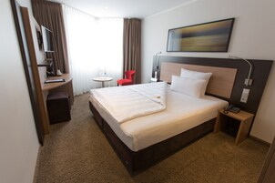 Habitación de hotel con una cama grande, un escritorio, una silla, una mesita y un cuadro en la pared.