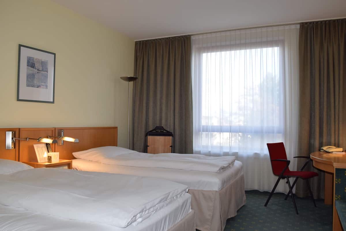 A hotel room with two beds, a desk with a chair, a lamp, and a window with curtains.
