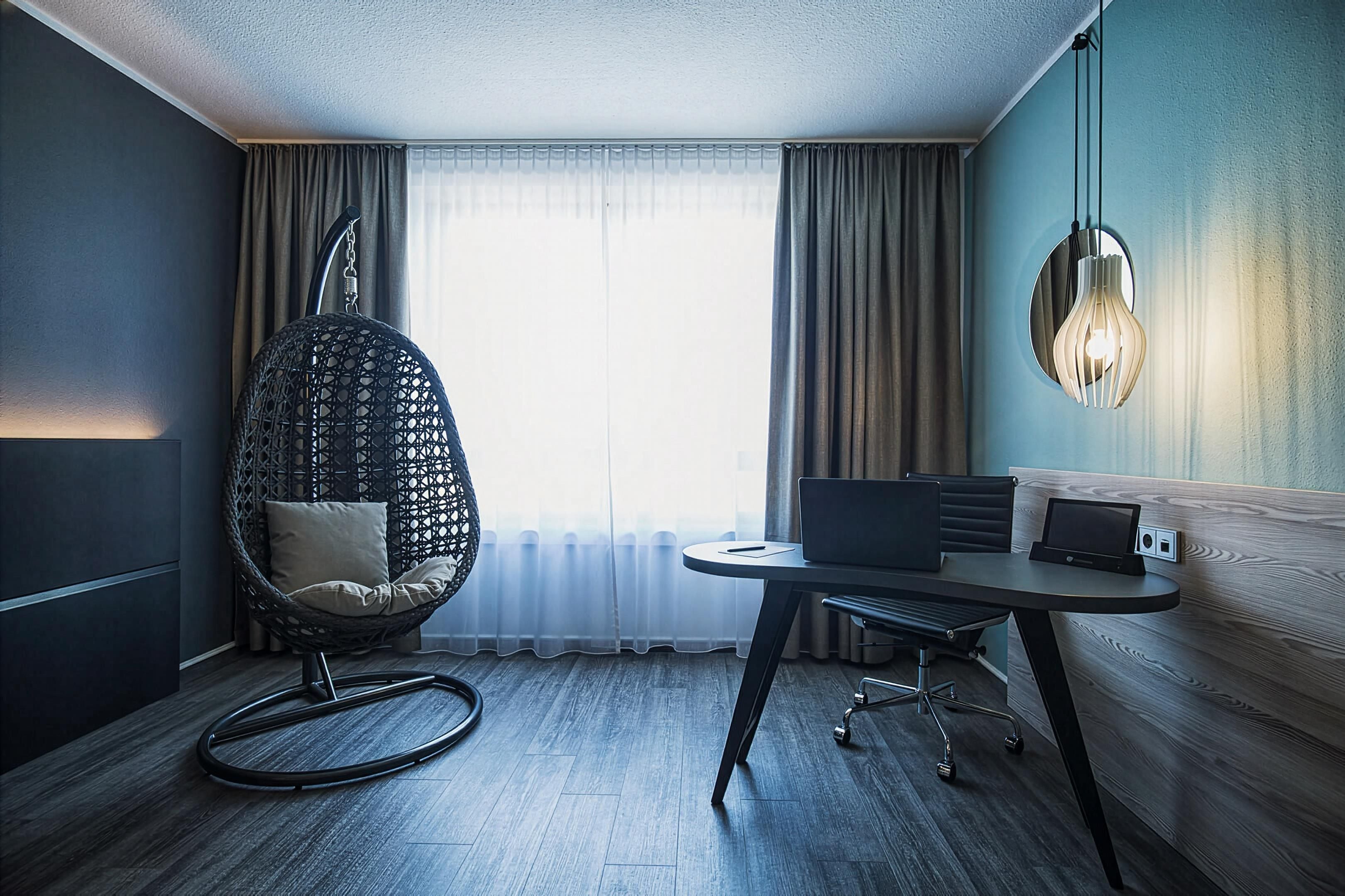 A modern hotel room with a hanging chair, a round table with a laptop, and a sofa.