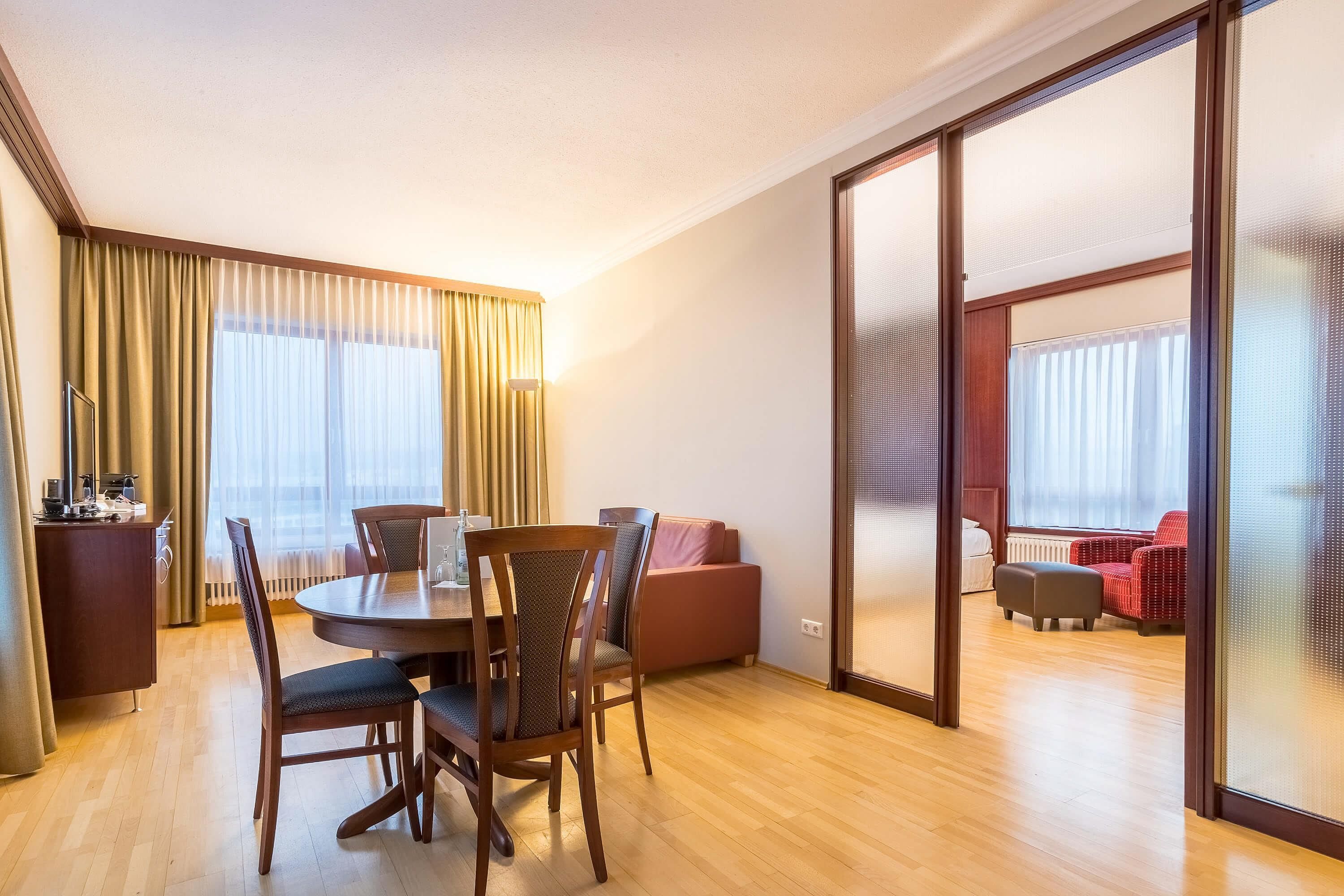Een hotelkamer met een eettafel, stoelen, een bank en een schuifdeur naar een balkon.