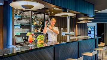 A bar area with a bartender, shelves of liquor bottles, and a bar counter with stools.