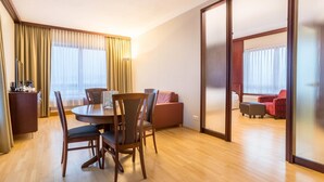 Een hotelkamer met een eettafel, stoelen, een bank en een schuifdeur naar een balkon.