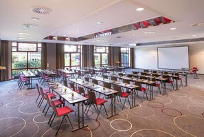 Ein Konferenzraum mit mehreren Tischen und Stühlen, großen Fenstern und einer Projektionsleinwand.