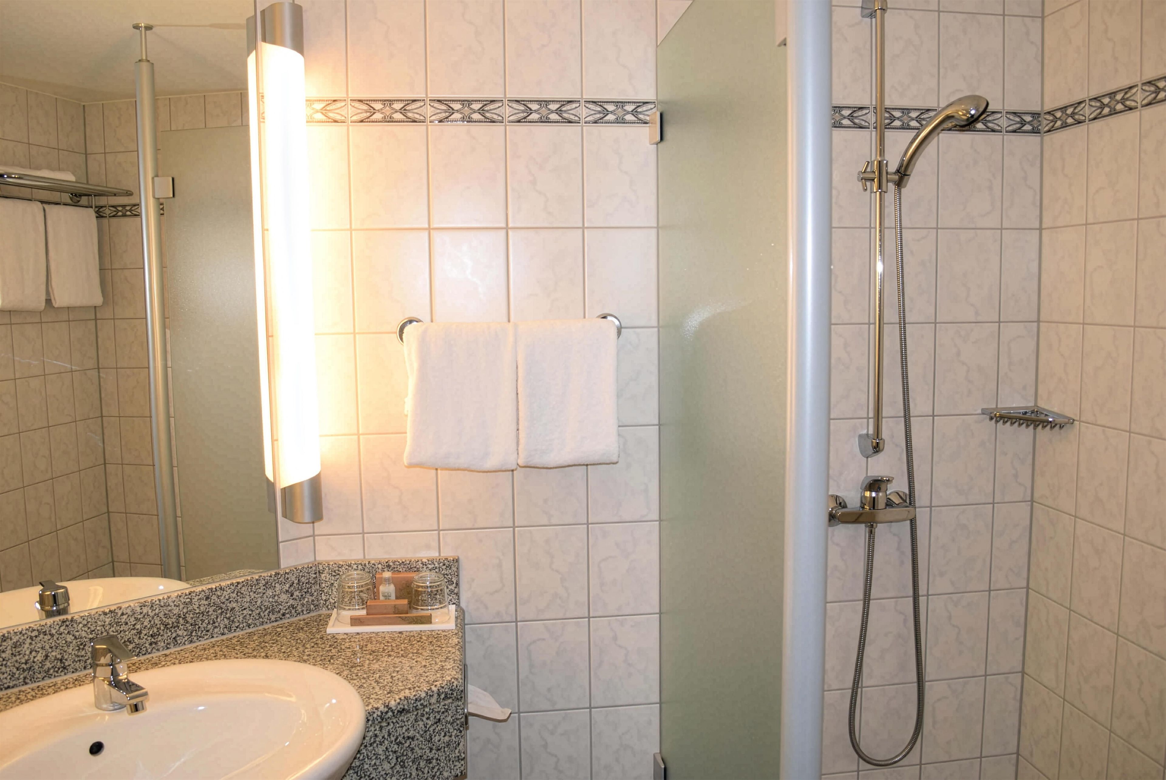 Ein Badezimmer mit Waschbecken, Spiegel, Handtuchhalter und Dusche.