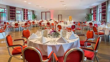 A banquet hall with round tables, red upholstered chairs, and white tablecloths.