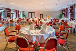 Ein Bankettsaal mit runden Tischen, rot gepolsterten Stühlen und weißen Tischdecken.