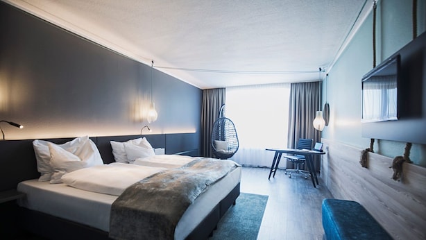 Een moderne hotelkamer met een groot bed, een bureau, een stoel en een hangstoel.