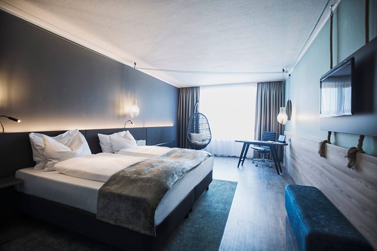 A modern hotel room with a large bed, a desk, a chair, and a hanging chair.
