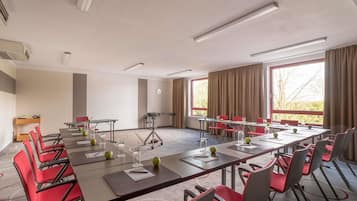 Un salón de conferencias con una larga mesa, sillas rojas y un amplio ventanal con cortinas.