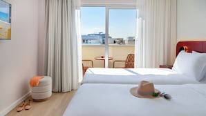 Hotellihuone, jossa on sänky, pieni pyöreä pöytä, tuoli ja ikkunasta avautuva näkymä kaupungin ylle.