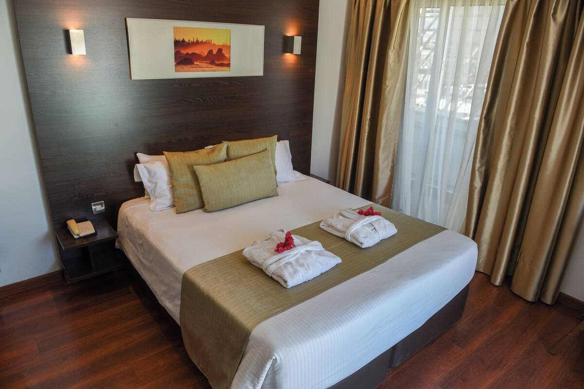 A hotel room with a large bed, a bedside table with a phone, and a painting on the wall.