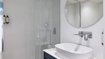 A modern bathroom with a glass shower enclosure, a white sink, and a round mirror.