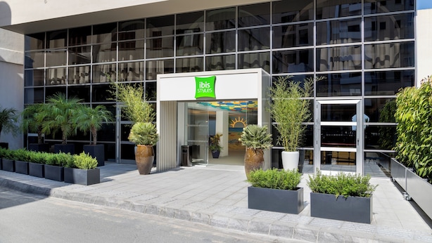 Moderni rakennus, jossa on lasijulkisivu, ja sen edessä on kyltti, jossa lukee »ibis Styles», sekä ruukuissa olevia kasveja.