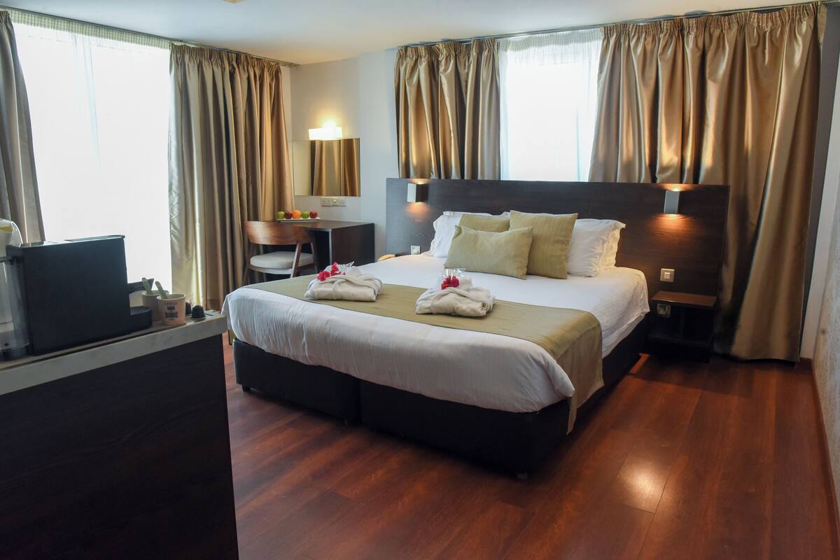 A hotel room with a large bed, a desk with a chair, a TV, and a window with curtains.