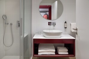 A modern bathroom with a glass shower enclosure, a white sink with a red countertop, and a mirror above the sink. - ibis Styles Larnaca Finikoudes Beach (Larnaca)