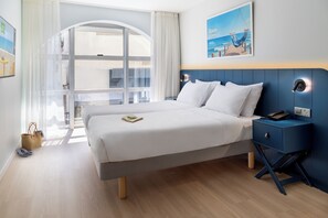 Une chambre d’hôtel avec un grand lit, une table de chevet, un bureau et une vue sur l’océan par la fenêtre.