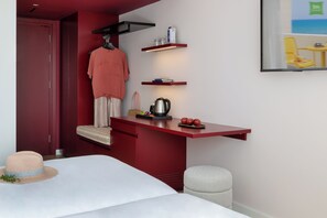 Een compacte kamer met een bed, een bureau met stoel, een kapstok en een klein krukje.